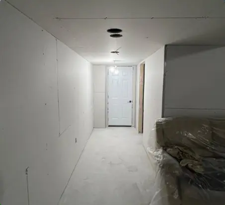 Narrow basement hall boarded, with the stairs wrapped in plastic