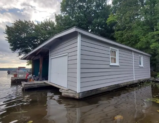 Grey boathouse with white trim on the lake, freshly painted